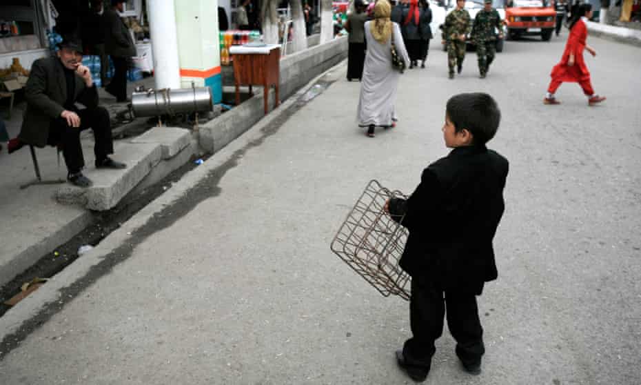 A child wearing a suit carries a crate through a street bazaar in Osh city, Kyrgyzstan 