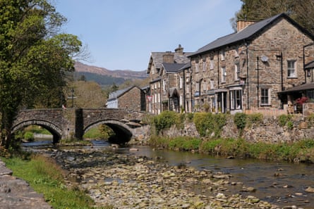 Stone cottages next to an arched stone bridge across a small river in the village of Beddgelert.
