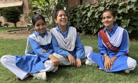 Three Pakistani schoolgirls in Shalwar kameez uniform sitting on a lawn