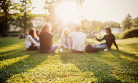 A group of young people sitting on the grass in a park, with the glare of the sun blurring their faces