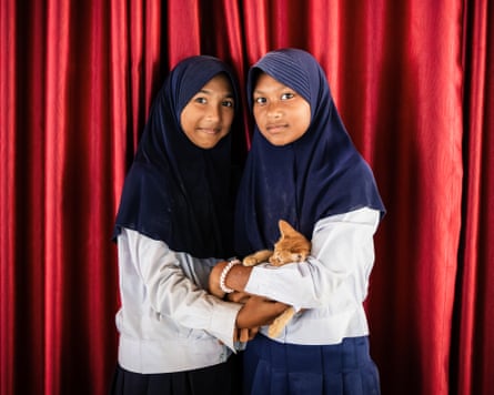 Two students pose in front of a red curtain with a ginger kitten