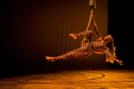 a woman leans back while holding herself in midair from aerial silk