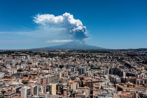 A volcano with smoke above it with the city of Catania in the foreground