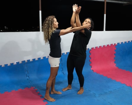 Two woman stand on mats demonstrating a martial arts move