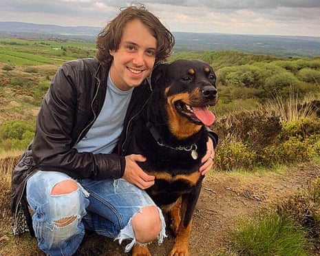 Oliver Robinson, in ripped blue jeans, black leather jacket and light-blue t-shirt, cuddles his dog while on a walk outdoors