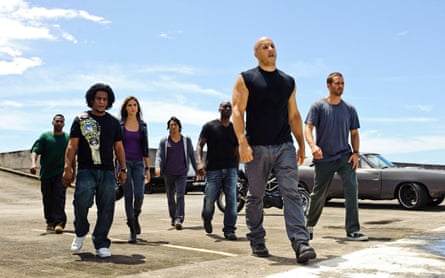 A group of people walk across a rooftop parking lot, led by Vin Diesel