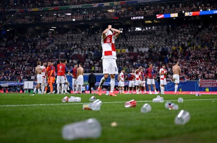 Plastic beer cups lie on a football pitch after a match with players still on the pitch