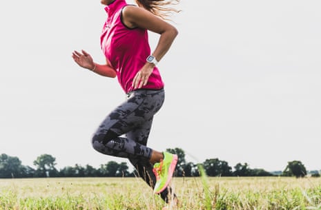 Young woman running fast in rural landscape wearing bright pink shirt, black leggings and green trainers