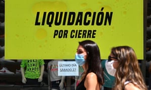 Women wearing masks walk by the window of a store offering a final sale before closing in Madrid.