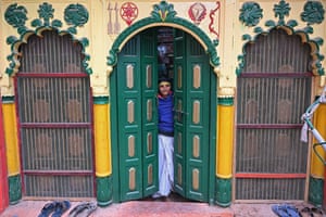 A boy with a painted forehead looks out from between two partially opened doors. Above him are ornate coloured carvings