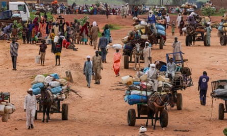 People walk with their belongings on dusty terrain