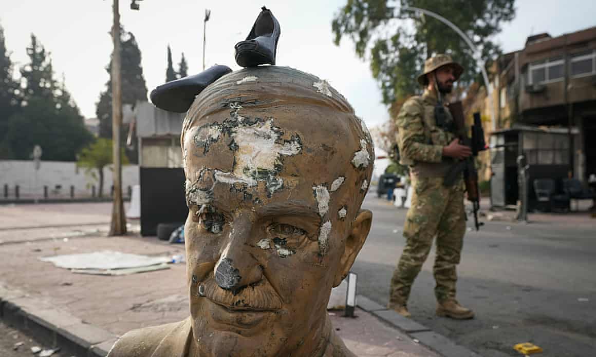 An opposition fighter in military uniform stands next to a broken bust of the late Syrian President Hafez Assad in Damascus.