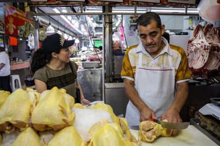 person wearing a black cap speaks with another person wearing a white apron in a butcher shop