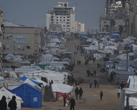 Palestinian people walking in the rain past war-damaged buildings and makeshift shelters in Gaza City on Sunday.