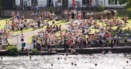 People swimming and gathered on the banks of a lake.