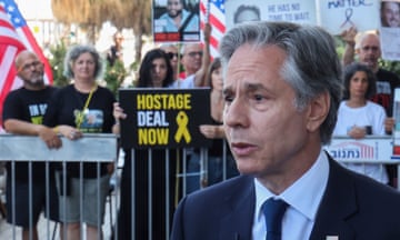 Antony Blinken speaks to the media: he is seen in front of a crowd who are holding signs with messages such as Hostage Deal Now and placards with pictures of hostages. Several US flags can be seen.