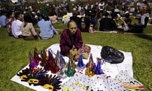 An elderly woman waits for customers as she sells fancy hats and masks for New Year's celebration at the Inya Lake park in Yangon, Myanmar