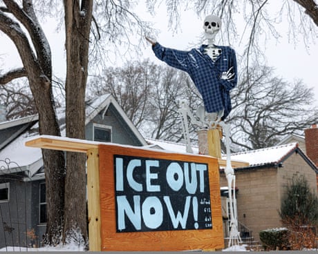toy skeleton wearing flannel shirt stands above sign that reads