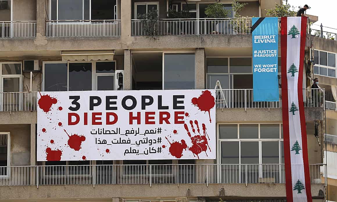 A man, right, hangs a giant Lebanese flag on a building that was damaged during the last year seaport blast during a one year commemoration in Beirut, Lebanon, Wednesday, 4 August, 2021.