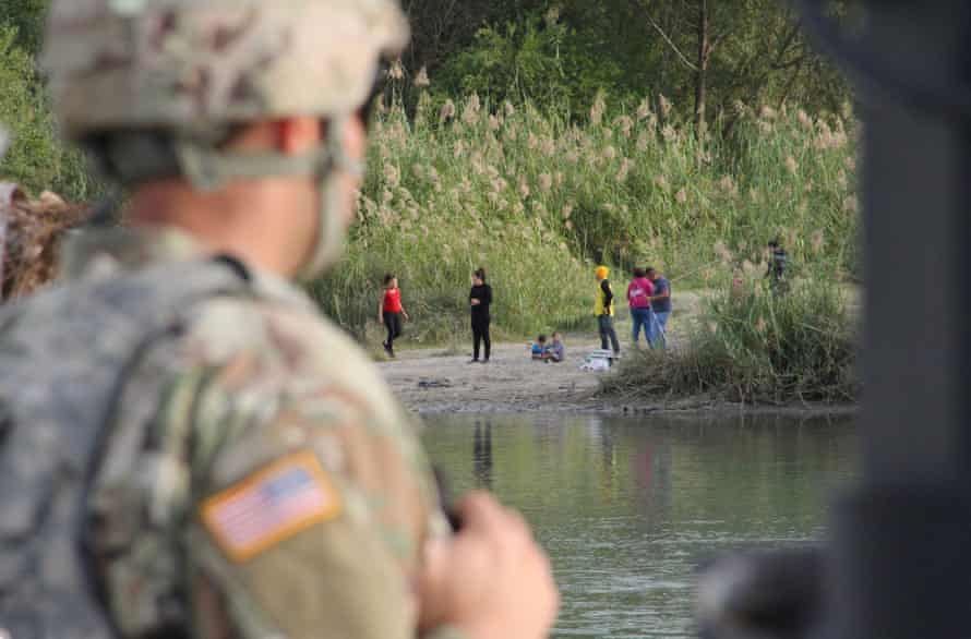A soldier looks across the Rio Grande River from Laredo, Texas, into Nuevo Laredo, Mexico, where a group of people hang out on the river bank.