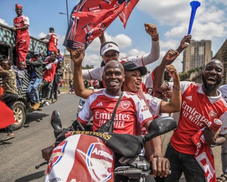 Arsenal supporters wearing jerseys and waving flag gather to celebrate the club’s Premier League title win.