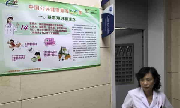 A hospital worker walks past a poster with information on rabies vaccine in Beijing, China.
