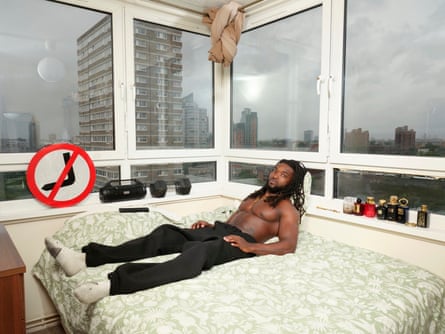 Roberto photographed lying on the bed in his room in front of windows that reveal grey skies and a city scene
