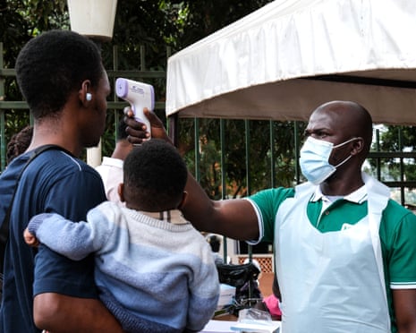 A health official in a face mask uses a handheld thermometer to check the temperature of people entering a facility