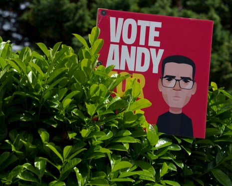 A red campaign poster reading VOTE ANDY with a cartoon illustration of Burnham is displayed among green bushes