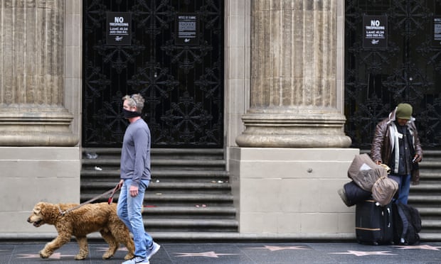 A man wearing a mask walks his dog past a homeless man along Hollywood Boulevard in Los Angeles.
