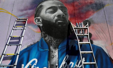 A mural of the late rapper Nipsey Hussle is in process. Two ladders lean against the wall, their steps lined with spray paint cans.