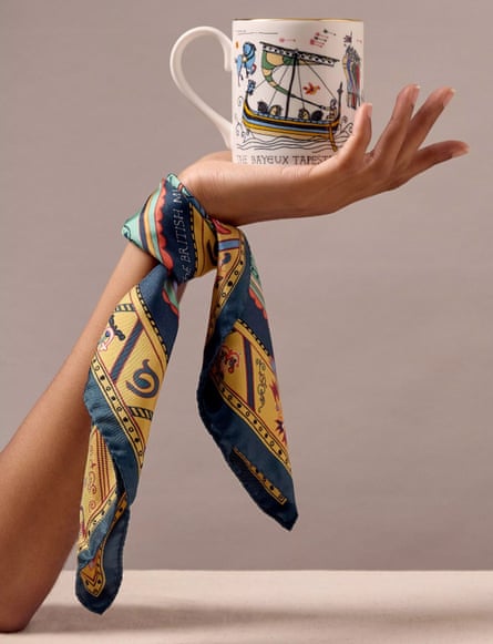 An arm with a silk scarf tied at the wrist and with a Bayeux tapestry mug in the palm of the hand