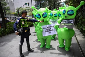A security guard points as he stands in front of protesters wearing green alien costumes and holding placards including ‘All beings have feelings’ and ‘Stop eating your fellow earthlings’