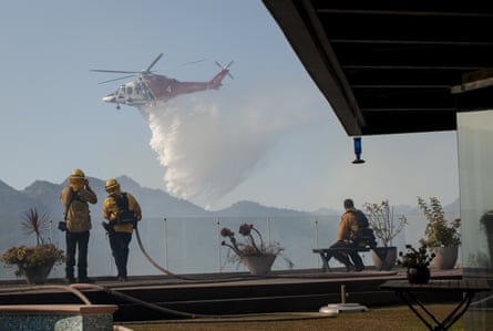 Firefighters watch from a home in the Pacific Palisades area as a helicopter drops water on a wildfire.