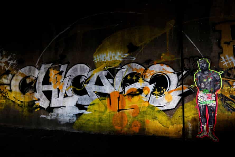 A mural spells out ‘Chicago’ in white with pops of orange and yellow next to a depiction of Kanye West in black and white wearing only shorts.