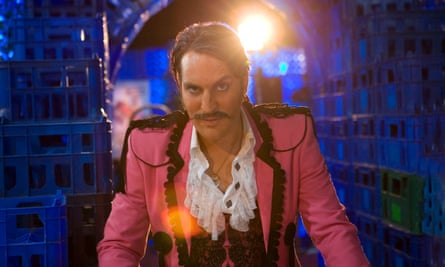 Noel Fielding in Bunny and the Bull. He is in a dark blue room and wearing a bright pink jacket over a white shirt