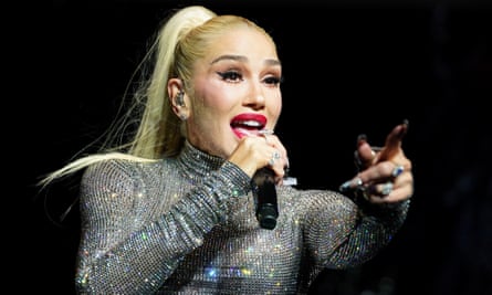 White woman holding microphone in right hand points with left hand