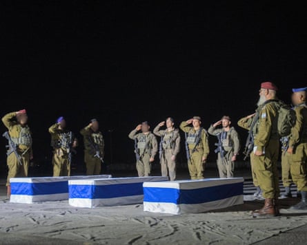 Soldiers salute over three coffins draped in blue and white