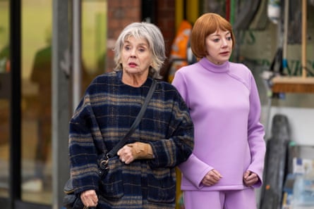 A woman with grey hair in a plaid coat standing next to a woman with red hair in a purple suit