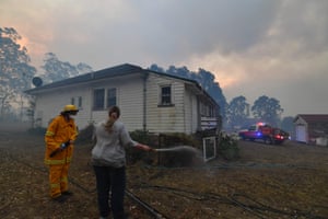 A resident tries to hose down her home in the hope of saving it from nearby bushfires around the town of Nowra.