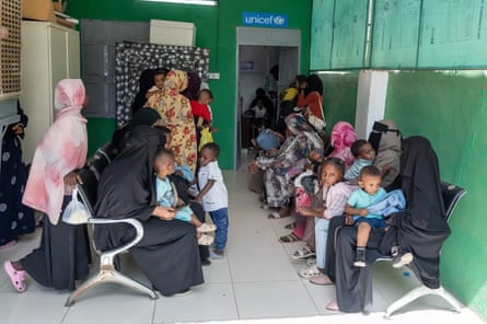 Women and children crowd into what appears to be a waiting room with rows of chairs