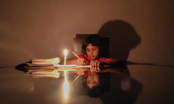 A child studies besides a lit candle at her residence during a power cut in Biyagama, a suburb of the capital Colombo