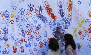 Children stamp their hands with paint on a paper wall during a Podemos party rally in Madrid.