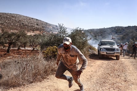 A Palestinian farmer and foreign volunteers flee as the Israeli army throws teargas canisters as they harvest olive groves near Ramallah in the West Bank.