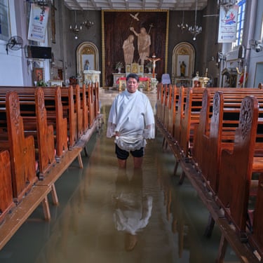 A man stands knee-deep in flood water in the isle of a church, which wooden pews to either side