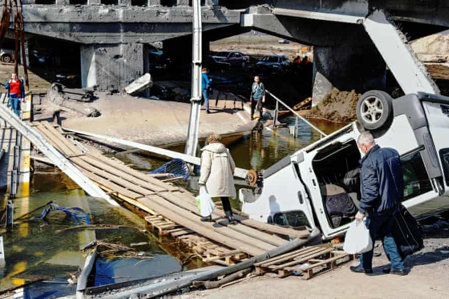 A woman crosses a temporary wooden bridge beside the destroyed Irpin Bridge in Hostomel.