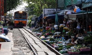 A train approaches a station platform lined with market displays of fruit, vegetables and flowers