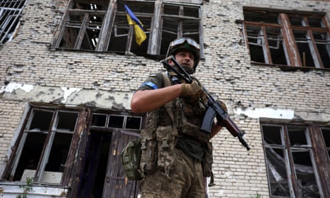 A Ukrainian serviceman stands in front of a heavily damaged cultural centre with a gun