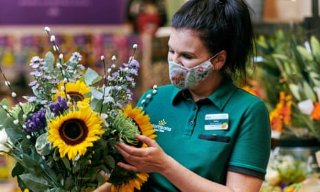 A woman in a green Morrisons uniform holding a bunch of flowers