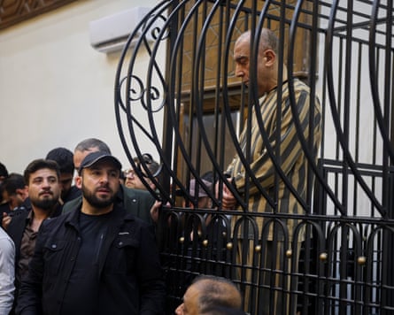 Atef Najib sits in the defendants’ cage as a crowd of people look on